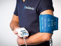 Ein Mann in einem ComService-Shirt hat ein Bludruckmeßgerät an seinem linken Arm