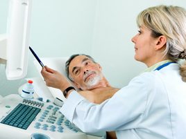 Eine Ärztin deutet mit einem Stift auf den Bildschirm eines Ultraschallgerätes. Ein Mann liegt mit nacktem Oberkörper auf dem Behandlungsliege.