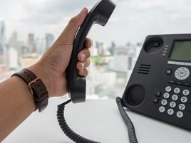 Eine Männerhand hebt den Hörer einer modernen Telefonanlage ab.